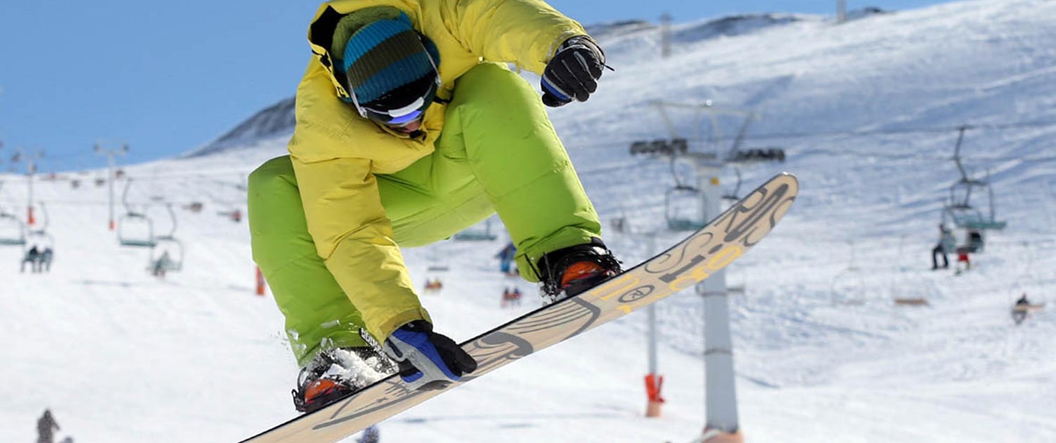 A person in a yellow jacket jumping on a snowboard